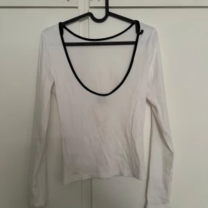 Vit långärmad topp med djup rygg - Säljer en vit långärmad topp med djup urringning i ryggen och svarta kanter. Snygg och enkel modell som passar till mycket. Tunn och mjuk i materialet.