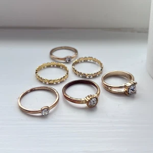 Sex ringar i guld- och silverfärg - Säljer ett set med sex ringar i guld- och silverfärg. Fyra ringar har en klar sten framtill och två ringar har ett mönster med små hjärtan runt om. Perfekta att mixa och matcha på olika fingrar. Olika storlekar. Skickas i den lilla plastförpackningen på sista bilden.