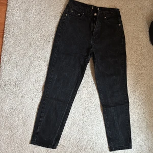 Svarta jeansbyxor med rak passform - Säljer ett par svarta jeansbyxor med klassisk femficksdesign och raka ben. Byxorna har hög midja, dragkedja och knapp framtill. Perfekta till en avslappnad stil och funkar året runt.