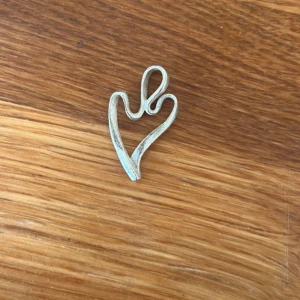 Äkta silver hjärthänge - Unikt hänge i i äkta silver i form av ett stiliserat hjärta med en snirklig design. Perfekt att använda som berlock till halsband eller armband. Silverfärgad metall ger en modern och stilren känsla.