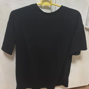 Svart t-shirt med tryck från SHEIN - Cool svart t-shirt från SHEIN med stort tryck på ryggen där det står 'MOTIVATED ATTITUDE' och en orange X över texten. T-shirten har rund hals och korta ärmar. Perfekt för en avslappnad och trendig stil.