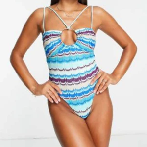 Missoni liknande baddräkt från River Island - Säljer en snygg baddräkt från River Island med Missoni mönster i turkos, blått, lila och vitt. Baddräkten har smala axelband och en rund öppning framtill. Helt ny med intim lapp och prislapp kvar! 