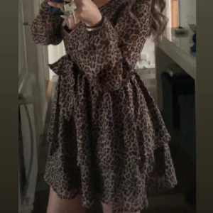 Leopardmönstrad omlottklänning med volang - Säljer en leopardmönstrad kortklänning från nakd med omlottmodell och volangdetaljer. Klänningen har långa ärmar och knyt i midjan för en snygg passform. Perfekt för dig som vill sticka ut lite extra!