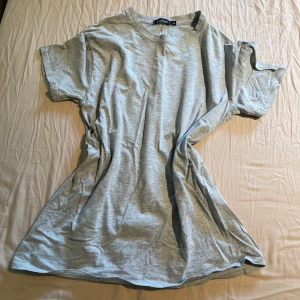 Grå t-shirt med tryck från Boohoo - Säljer en grå t-shirt från Boohoo med stort tryck på ryggen föreställande en hand och en fjäril samt texten 'Ye Saint West California'. T-shirten har korta ärmar och är i mjukt bomullsmaterial. Perfekt för en chill och avslappnad stil.