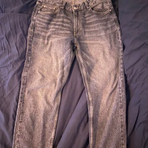 Grå straight jeans - Säljer ett par grå jeans med klassisk femficksdesign och raka ben. Jeansen har normal passform och stängs med dragkedja och knapp. Perfekta till vardags för en avslappnad stil.