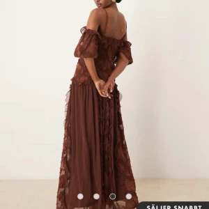 Brun långklänning med volang och spetsdetaljer - Oanvänd balklänning med lappen kvar i storlek 34 men passar även mig i 36. ❤️nypris 1000