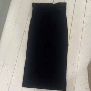 Svart sammetskjol med dragkedja - Säljer en svart långkjol i sammet med en diskret dragkedja bak. Kjolen har en rak och elegant passform som sitter snyggt i midjan. Perfekt för dig som gillar en stilren och klassisk look.