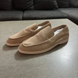 Beige loafers från Loro Piana - Säljer ett par stilrena beige loafers från Loro Piana, modellen Summer Walk. Skorna har en klassisk design med rund tå och platt sula. Tillverkade i mocka med diskreta sömmar och vit yttersula. Perfekta för en clean och avslappnad look. Pris :999kr