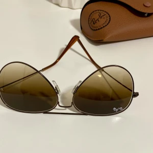 Bruna aviator-solglasögon från Ray-Ban - Säljer ett par Ray-Ban solglasögon. Aviator-modellen har bruna linser och inkluderar originalbågen. Det enda problemet är att det finns några repor på glasögonens bågar. Diamantsymbolen har ett bevakning i glasskydd.