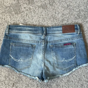 Blå jeansshorts 💞 - Säljer ett par blå jeansshorts från Superdry med fransig kant och rosa detaljer vid fickorna. Shortsen är lågmidjade💞36cm I midjan tvärs över