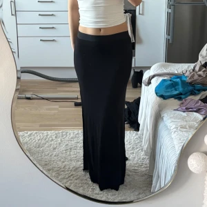 Svart långkjol med slits - Säljer en svart långkjol med hög midja och slits på sidan. Kjolen har en rak och tight passform som sitter snyggt längs kroppen. Perfekt att styla med crop tops eller stickade tröjor. OBS! Bra skick!! Ej nyskick!! 