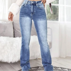 Blå bootcut jeans med slitningar - Säljer ett par blå bootcut jeans med hög midja och snygga slitningar framtill. Jeansen har klassiska fem fickor och dekorativa detaljer på bakfickorna. Perfekta för dig som gillar en trendig och bekväm stil.