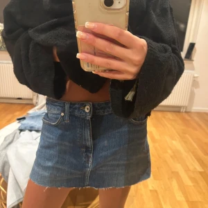 Jeanskjol i klassisk blå denim - Säljer en kort jeanskjol i klassisk blå denim med rå kant nertill och femficksmodell. Kjolen har knapp och dragkedja framtill samt bälteshällor. Perfekt för dig som gillar en enkel och tidlös stil.