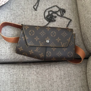 Brun axel/medje-väska - Säljer en brun axelväska  med klassiskt mönster och kedjerem. Väskan har ett kuvertformat lock och insida med rutigt tyg. Perfekt för dig som vill ha en snygg accessoar med lyxig känsla. Bara att skriva vid frågor och priset kan såklart diskuteras!