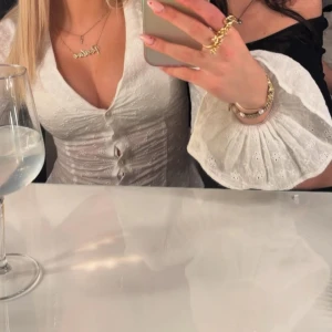 Vit blus med broderade detaljer och knappar - Säljer en vit blus med djup v-ringning och fina broderade detaljer. Blusen har långa ärmar med volang och knappar framtill. Perfekt för dig som vill ha en romantisk och trendig look. Säljer då den är för stor💕