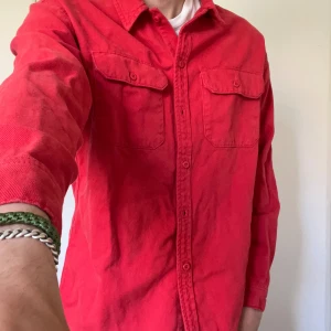 Röd skjorta från ZARA - Snygg röd skjorta från ZARA med klassisk krage och två bröstfickor med lock. Skjortan har långa ärmar och stängs med knappar framtill. Perfekt för dig som vill sticka ut lite extra. Är snarare overshirt eller jacka då det är jeans material.