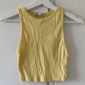 Gul croppad linnetopp från Zara - Säljer en ljusgul ribbad croppad linnetopp från Zara. Toppen är ärmlös med rund halsringning och har en tight passform. Perfekt för varma dagar och enkel att matcha med jeans eller kjol.