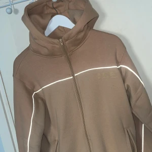 Beige streetwear hoodie  - Säljer en beige hoodiejacka från ICE med dragkedja och huva. Jackan har vita och reflekterande detaljer. Otroligt varm och skön hoodie.