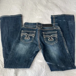 Blå jeans med broderade bakfickor från Blue Monkey - Snygga blå jeans från Blue Monkey med kontrastsömmar och broderade detaljer på bakfickorna. Jeansen har låg midja och bootcut-passform. Skriv om ni har några frågor💕