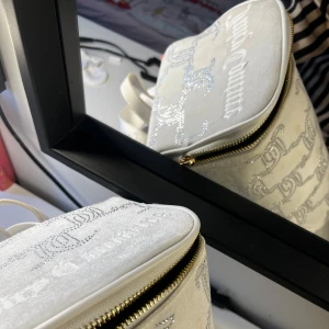 Vit ryggsäck från Juicy Couture med strassdetaljer - Säljer en vit ryggsäck från Juicy Couture med glittriga strassdetaljer och mönster. Väskan har guldfärgade dragkedjor, justerbara axelband med logga och ett innerfack med gulddetaljer. Perfekt för dig som gillar bling och vill sticka ut.
