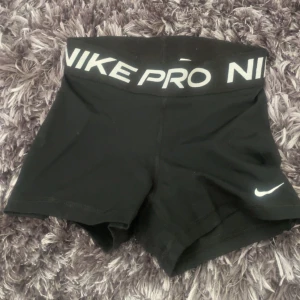 Svarta träningstights shorts från Nike Pro - Svarta tighta träningstights shorts från Nike Pro med bred resår i midjan och vit logga. Perfekta för gymmet eller löpning, men passar även perdekt för en avslappnad vardags look. Snygg och sportig design med hög komfort.
