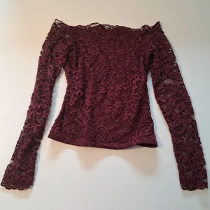 Vinröd spetsblus från H&M - Säljer en vinröd långärmad blus från H&M i vacker spets. Blusen har offshoulder-modell och ett blommigt spetsmönster.