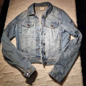 Ljusblå jeansjacka med knappar - Säljer en klassisk ljusblå jeansjacka från . Jackan har två bröstfickor med lock och knappar framtill. Den är croppad och har långa ärmar samt en snygg krage. Perfekt att slänga på sig till vardags! PRIS:150KR
