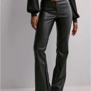 Svarta lågmidjade skinnbyxor med bootcut - Snygga svarta byxor i skinnimitation med bootcut-modell och låg midja. Byxorna har knapp- och dragkedjestängning framtill och sitter tight upptill med utsvängda ben. Perfekta för en trendig och stilren look.