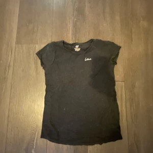 Svart t-shirt med broderad text från H&M - Svart t-shirt från H&M med liten broderad text 'love' på bröstet. Klassisk rund hals och korta ärmar. Perfekt basplagg med enkel och stilren design.