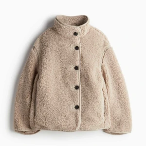 Beige teddyjacka med knappar - Mysig beige teddyjacka med knappar framtill. Perfekt för kyliga höst- och vinterdagar. Jackan har en hög krage och långa ärmar för extra värme. Den är i mycket bra skick och passar perfekt för en avslappnad stil. Slutsåld på hemsidan!
