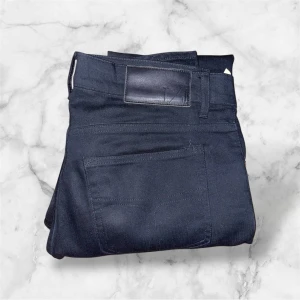 Svarta Tiger of Sweden jeans - Säljer ett par svarta jeansbyxor från Tiger of Sweden Jeans. Jeansen är raka/skinny och har en svart läderpatch bak i midjan. Storlek 📐 W29 L32. Nästan helt nya så bästa kvaliteten!!! Kontakta oss vid frågor🥂 