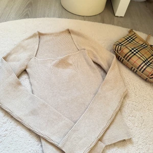 Beige ribbad långärmad topp - Säljer en beige ribbad långärmad topp med markerad byst och figurnära passform. Toppen har en snygg, modern design och är perfekt att styla till olika outfits.    ( Aldrig använd)