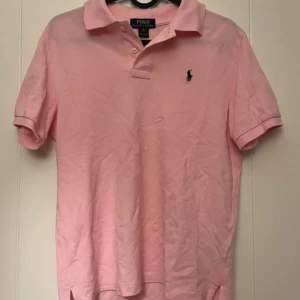 Ljusrosa pikétröja från Polo Ralph Lauren - Säljer en ljusrosa pikétröja från Polo Ralph Lauren med korta ärmar och krage. Tröjan har broderad logga på bröstet och är tillverkad i bomull. 