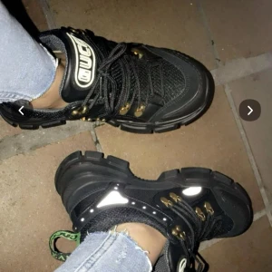 Svarta Gucci flashtrek sneakers strl 37 - Äkta Gucci flashtrek strl 37 (jag har i vanliga fall 38, funkar på mig). Har tyvärr inte kvitto kvar därav lågt pris. Har dustbag kvar. Få defekter, sparsamt använda. Ord. Pris 8000 :-. Pris går ej att diskutera. 