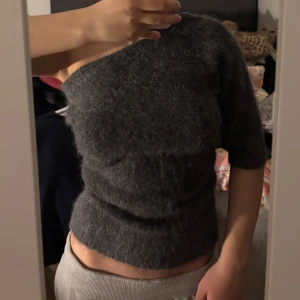 Mörkgrå fluffig tröja med kort ärm - Mysig mörkgrå tröja med fluffig yta och korta ärmar. Tröjan har en tight passform och är perfekt för dig som gillar en enkel men ändå trendig look. Passar bra till både jeans och kjol.