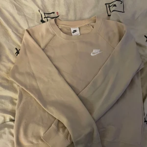 Beige sweatshirt från Nike ingår byxor!!!👖  - Säljer en beige sweatshirt från Nike med klassisk logga broderad i vitt på bröstet. Tröjan har rund halsringning och långa ärmar, perfekt för en avslappnad och sportig stil. BYXOR INGÅR.