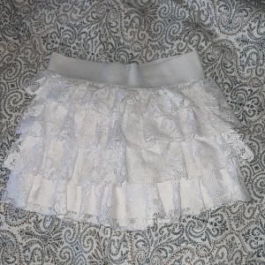 Vit volangkjol i spets - Säljer en söt vit kortkjoö med flera lager volanger i spets. Kjolen har bred resår i midjan. Kontakta för fler bilder på