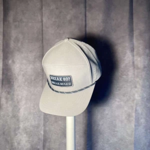 Beige keps med text - Snygg beige keps med patch framtill där det står 'BREAK 80? BREAK RULES!'. Klassisk form med böjd skärm och justerbar baksida. Perfekt accessoar för en avslappnad stil.