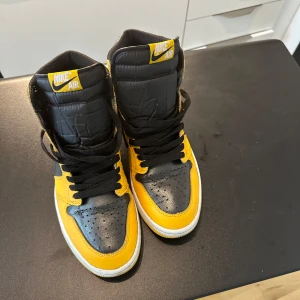 Nike Air Jordan 1 High svart/gul - Säljer ett par Nike Air Jordan 1 High i svart och gul med vita sulor. Klassisk hög modell med svart snörning och tydlig Air Jordan-logga på sidan. Perfekta för dig som vill sticka ut med färg och stil.