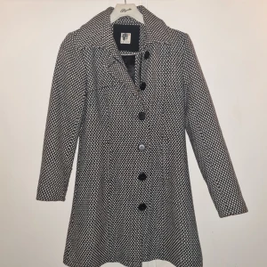 Svartvit mönstrad kappa från ICHI - Säljer en svartvit kappa från ICHI med grafiskt mönster. Kappan har klassisk krage, knäppning framtill med svarta knappar och är helfodrad med svart tyg. Långärmad och lätt utställd passform som ger en snygg siluett. PRIS:150KR