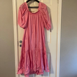 Rosa volangklänning med puffärm - Säljer en söt rosa klänning med volangkant och puffiga korta ärmar. Klänningen har en lös passform och är perfekt för sommarens alla tillfällen. Den har en fyrkantig ringning och är tillverkad i ett lätt material.