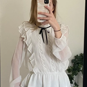 Vit spetsblus  - Fin spetsblus som är perfekt för en lite kyligare sommarkväll. Blusen har använts fåtal gånger och har inga defekter. Den är i storlek 152 och den svarta rosetten på kragen är borttagbar.