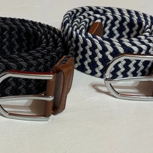 Randiga flätade herrbälten/Grischbälten - Flätade herrbälten i olika färger: svart/grå, blå/svart och blå/vit. Bältena har ett randigt mönster, bruna skinn-detaljer och ett stilrent silverfärgat spänne. Perfekt accessoar för att lyfta din grisch outfit.