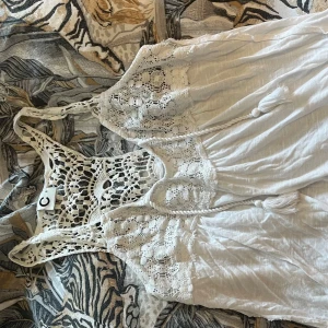 Vitt linne med spetsdetaljer - Superfint linne med vackra virkade spetsdetaljer upptill och i ryggen. Linnet har en avslappnad passform och tunna axelband. Perfekt för varma dagar och somriga tillfällen.