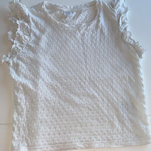 Vit T-shirt med volangärmar - Säljer en vit T-shirt med volangärmar, från Lindex Kids. Tröjan är i storlek för 146-152 cm. Jag säljer den, då den är för liten för mig. 