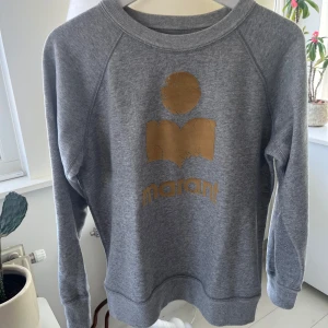 Grå sweatshirt från Isabel Marant Étoile - Grå sweatshirt med guldigt/gult tryck framtill från Isabel Marant Étoile. Storlek 40, den är i mycket bra skick och är använd fåtal gånger.            Inga slitningar!!                                                             Hör av i om ni vill ha fler bilder eller om ni har några frågor🤗