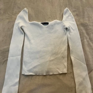 Vit ribbad långärmad topp från SHEIN - Säljer en vit ribbad långärmad topp från SHEIN med unik v-ringad halsringning och figurnära passform. Toppen har långa ärmar och är tillverkad i stretchigt material som sitter snyggt på kroppen.