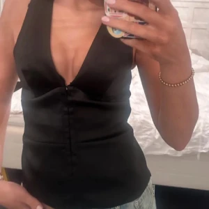 Svart v-ringad linnetopp - Säljer en svart linnetopp med djup v-ringning och knappar framtill. Toppen är ärmlös och har en figurnära passform, perfekt att styla med jeans eller kjol.