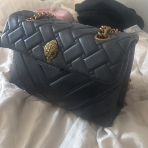 Svart quiltad axelväska med guldkedja - Säljer en svart quiltad axelväska med snygg guldfärgad kedja och dekorativt spänne framtill. Väskan har ett elegant och stilrent utseende, perfekt för att lyfta din outfit. Rymmer det viktigaste och passar till många tillfällen. Skit snygg, inga defekter!💖💖
