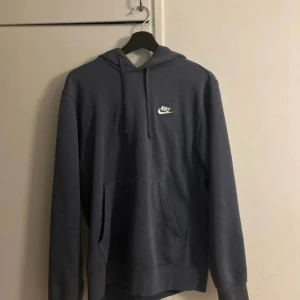 Blå hoodie från Nike - Säljer en klassisk blå hoodie från Nike med vit logga på bröstet. Tröjan har huva med dragsko och en stor magficka. Perfekt för en avslappnad stil och enkel att matcha med det mesta.
